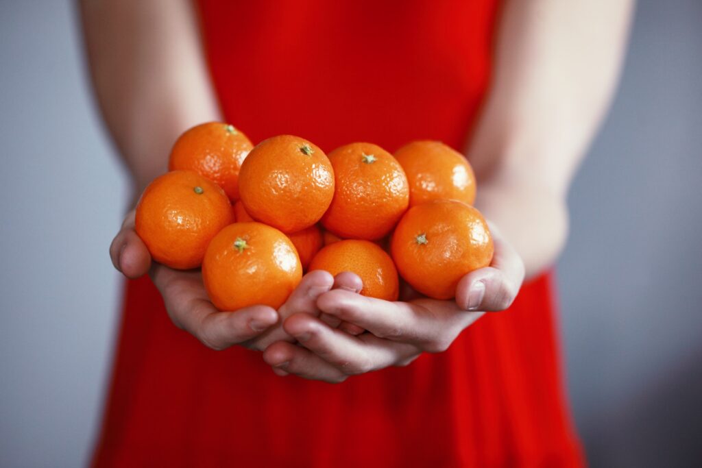 a person in a red dress holding many mandarins, abundance is a positive money mindset