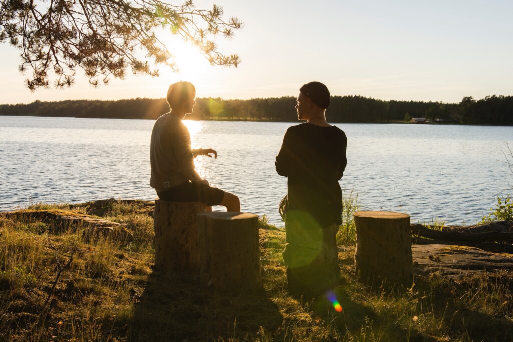 Two people sitting and talking by the lake side with a setting sun in the background